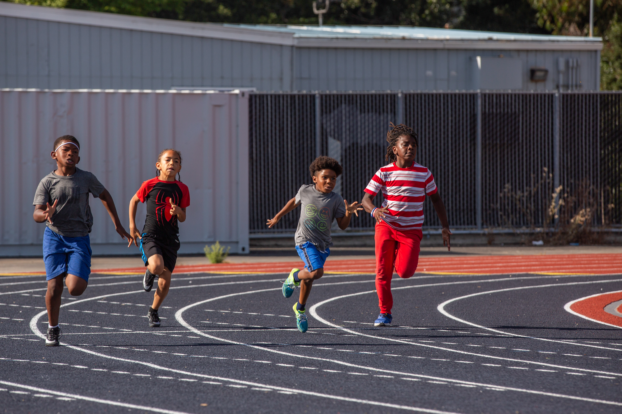 Four children run around a track.