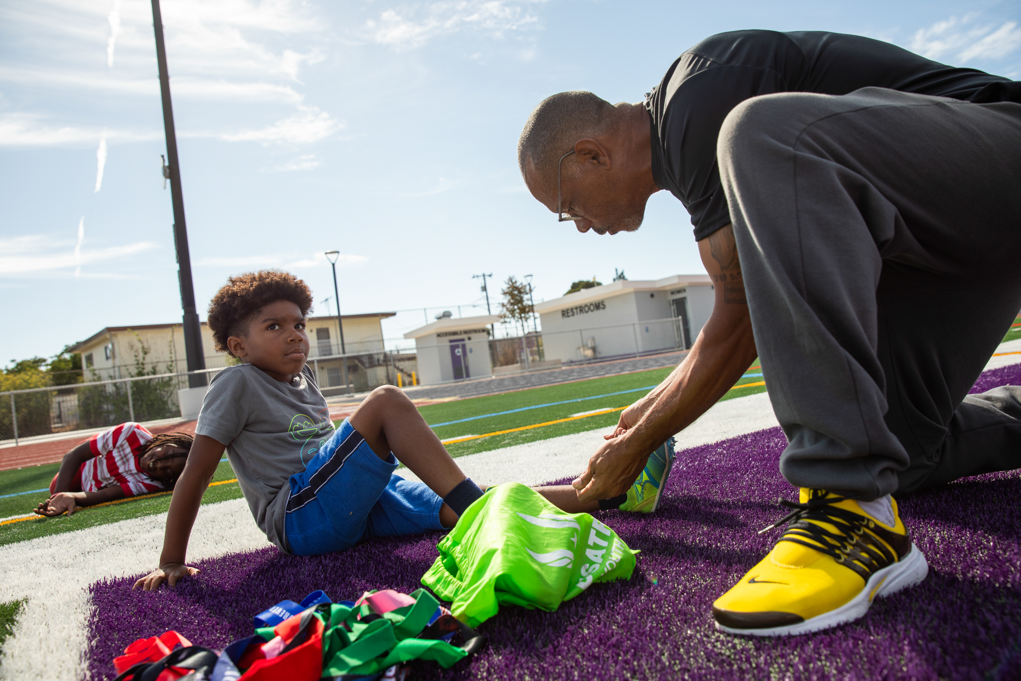 A man inspects the shoe of a child on a sports field.