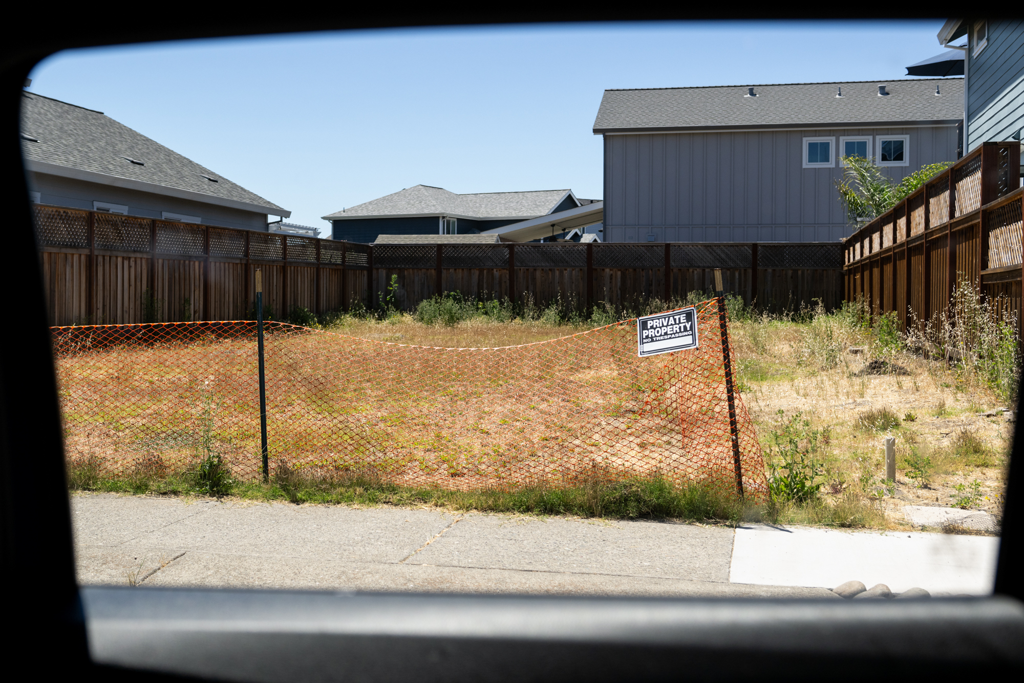 A large empty lot with overgrown grasses surrounded by houses.