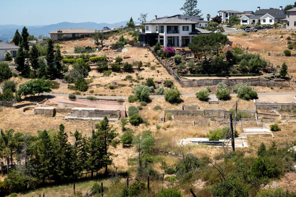 A hillside with the exposed foundations of several destroyed homes and a handful of newly built houses.