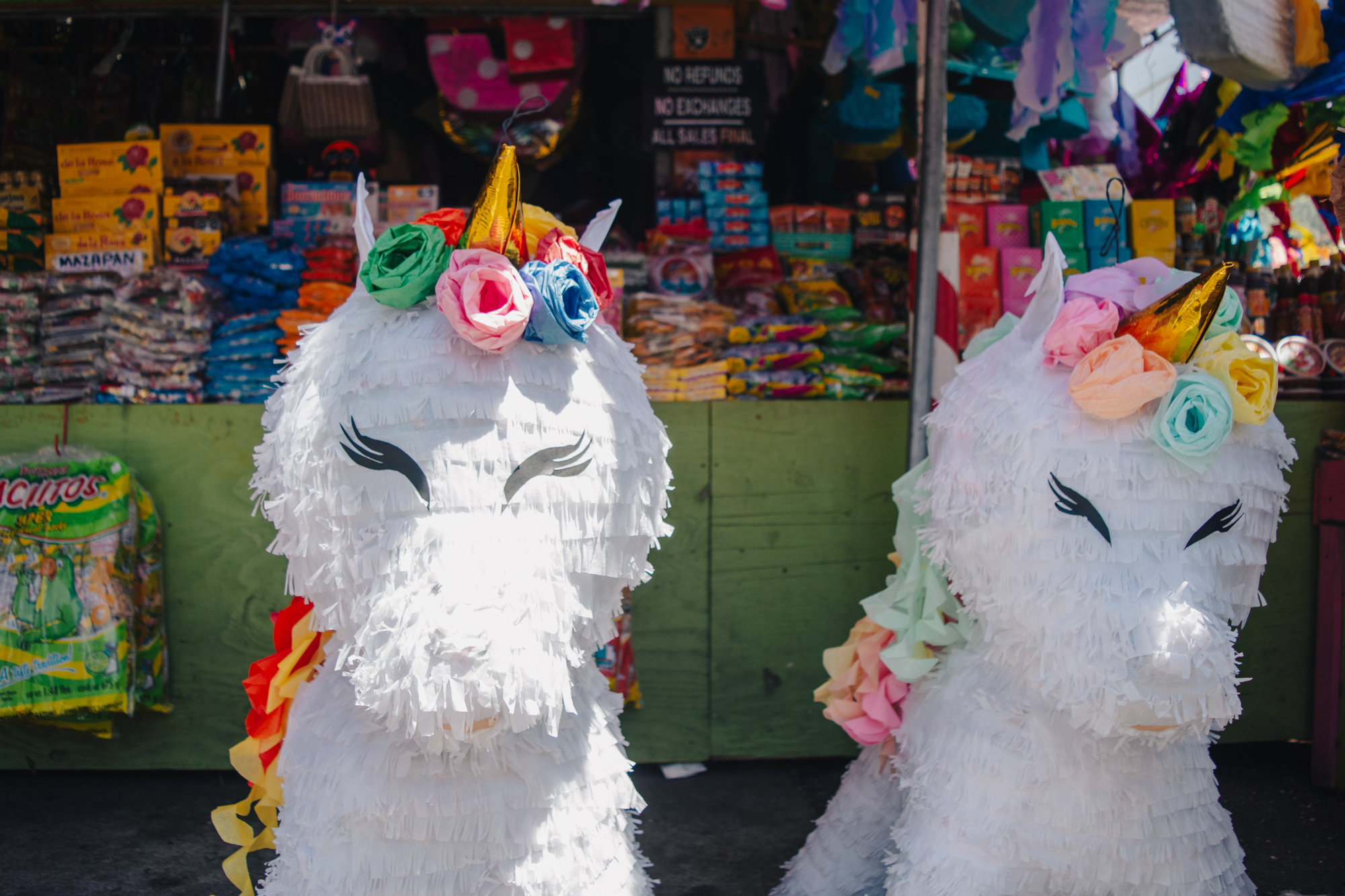 Two large white piñata unicorns in front of a stall full of wares.