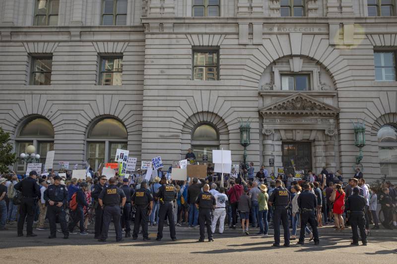 Police and protesters with sign stand in front of a San Francisco building.