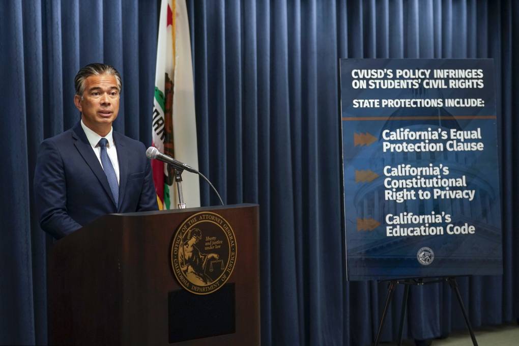 California's Attorney General Rob Bonta stands behind a podium. Next to him is a poster that state laws and codes that he says is being violated by a school district.