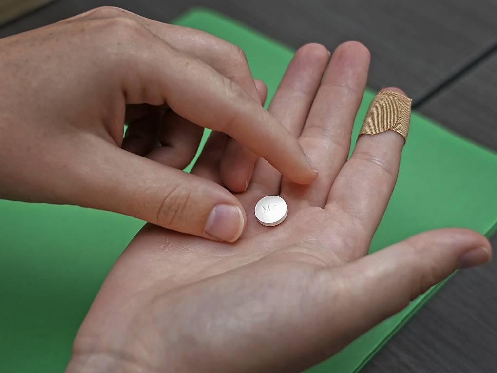 A person's hand drops a white pill into their other hand.