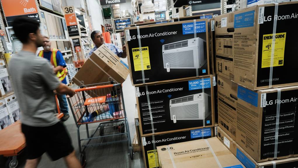 A man holds on to a shopping cart with a large box in it. Next to the man are images of a white air conditioning unit.