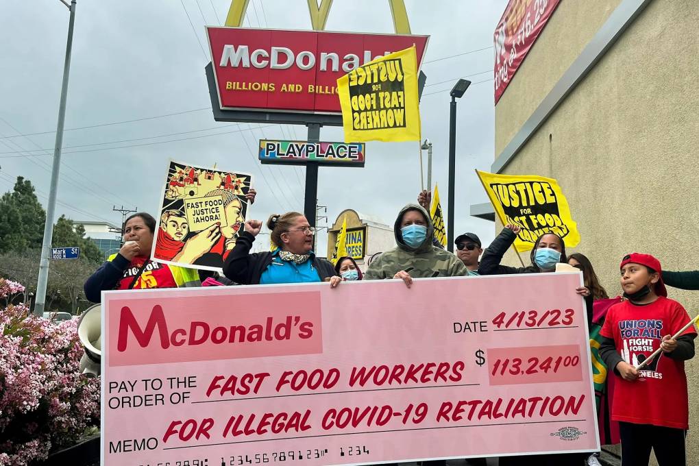 a group of people protesting outside a McDonald's hold a giant fake check addressed to 'fast food workers'
