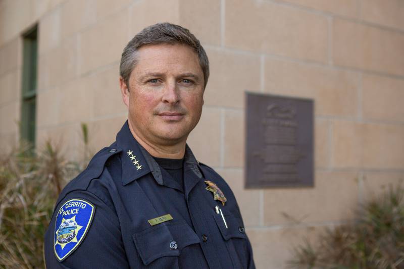 A man wearing a police uniform stands by a building outside.