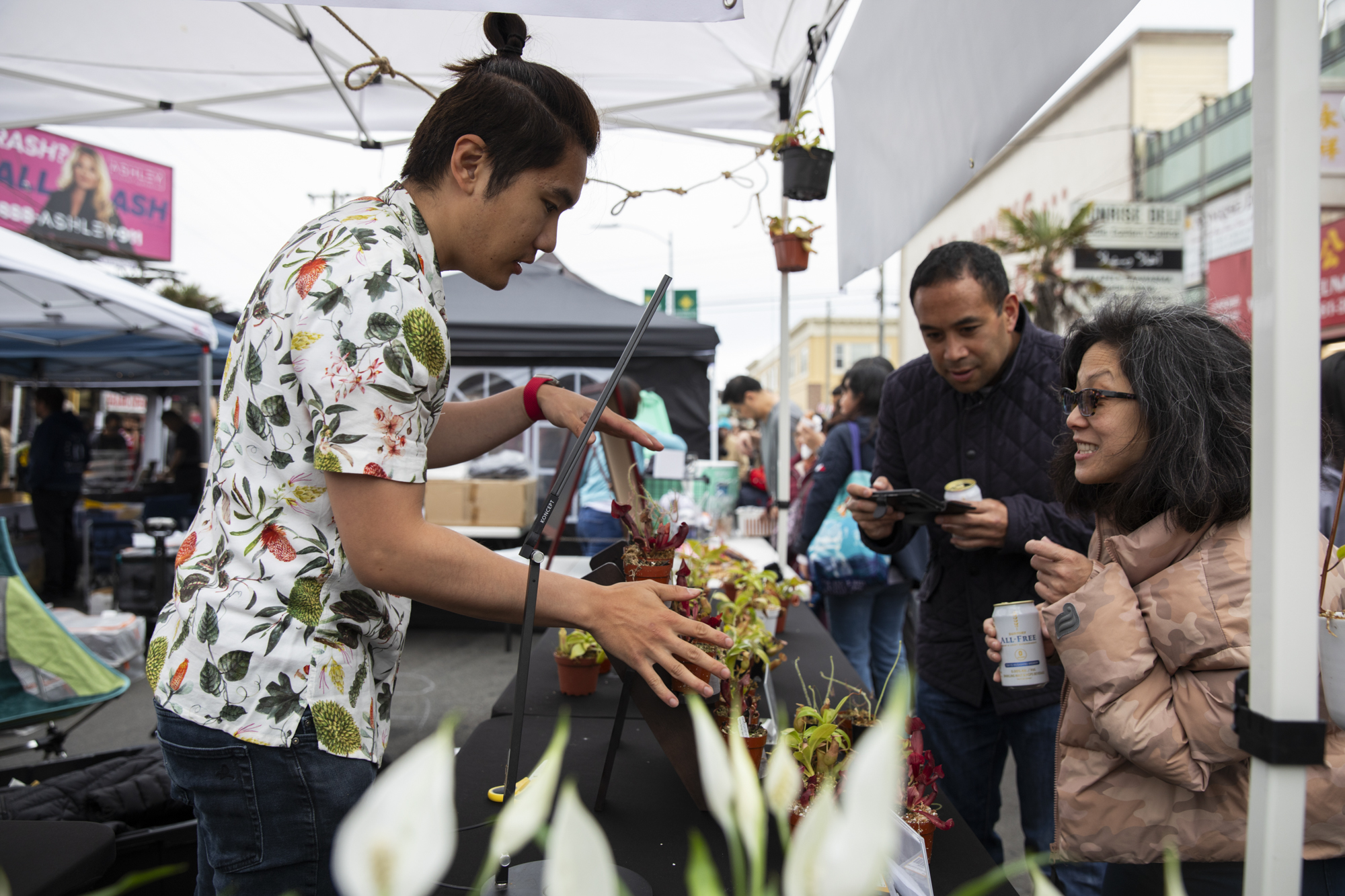 People interact with a vendor selling plants in an outdoor market.