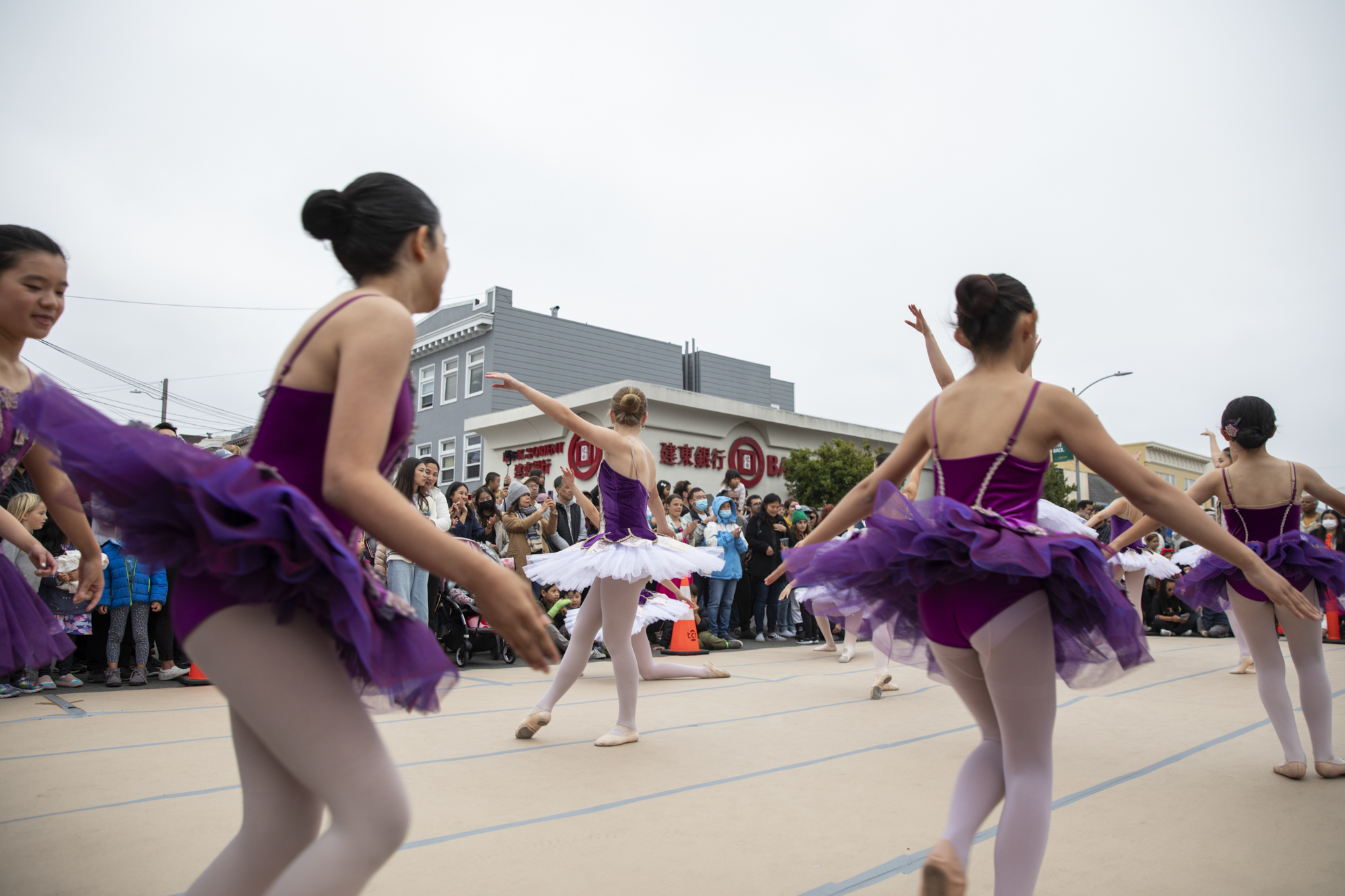 Young people in tutus perform for an audience outdoors.