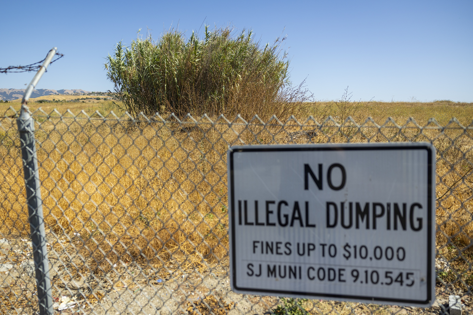 A sign on a chain link fence reading "No Illegal Dumping" in front of a large open field.