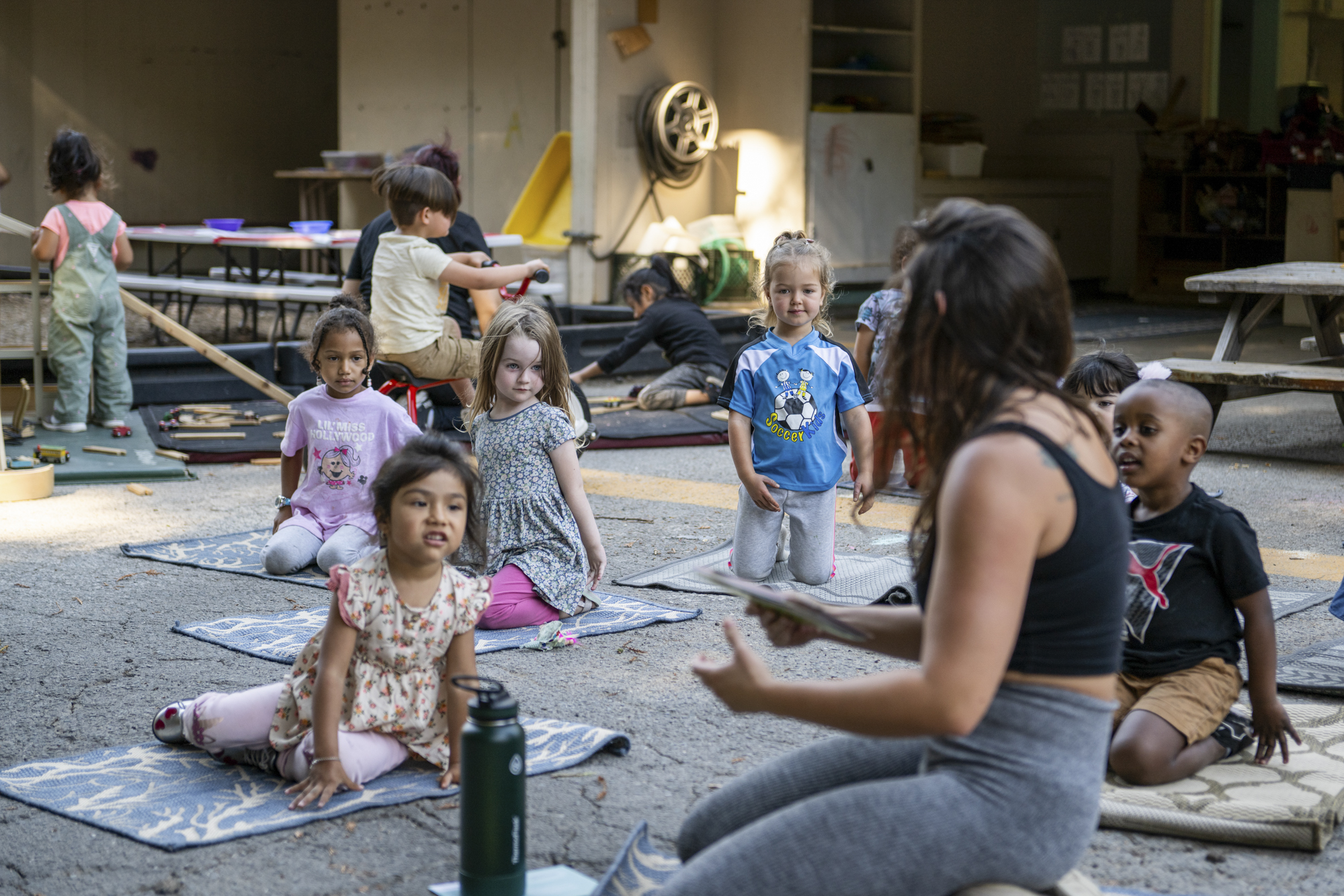 A group of children on mats watch an adult in front of them.