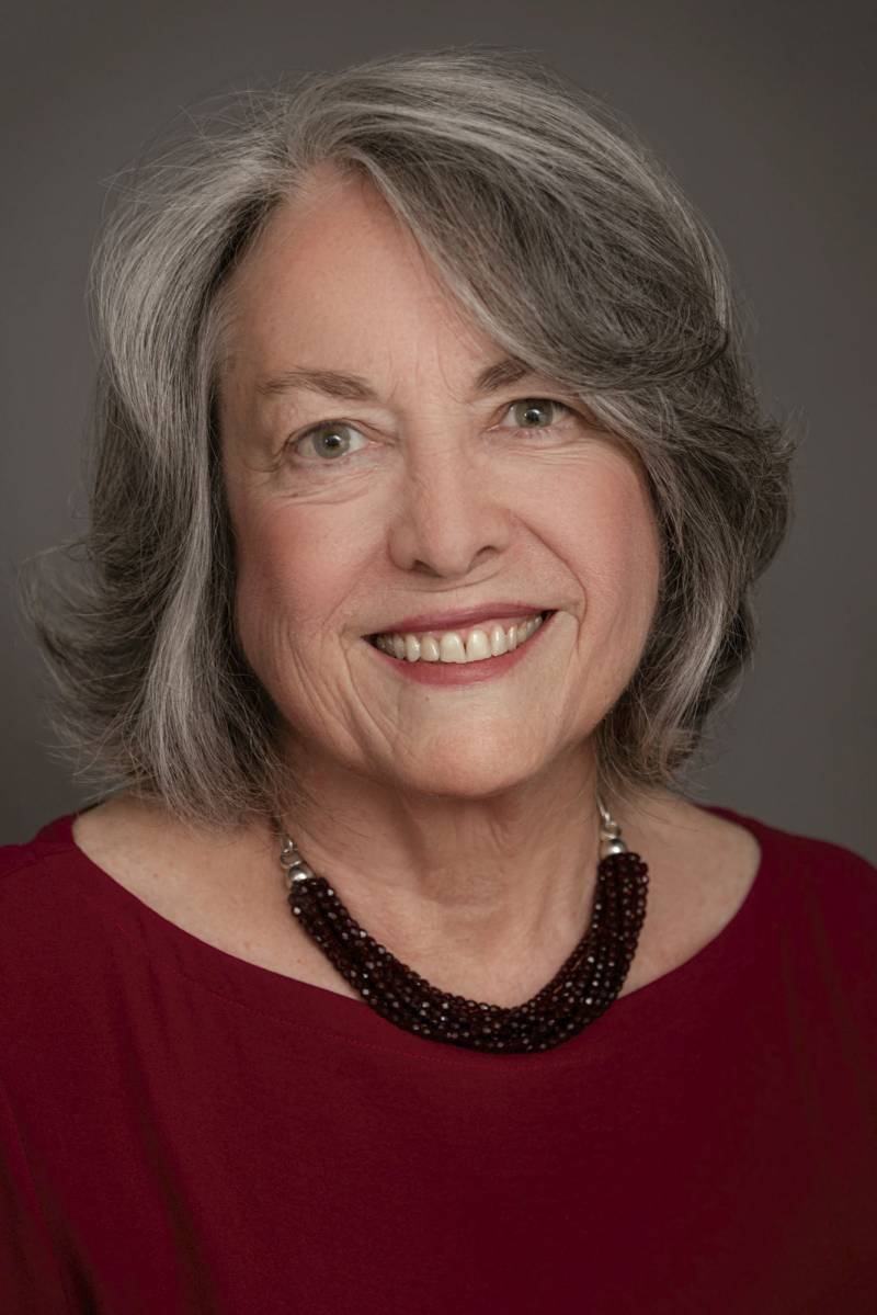 A person with long gray hair smiles at the camera.