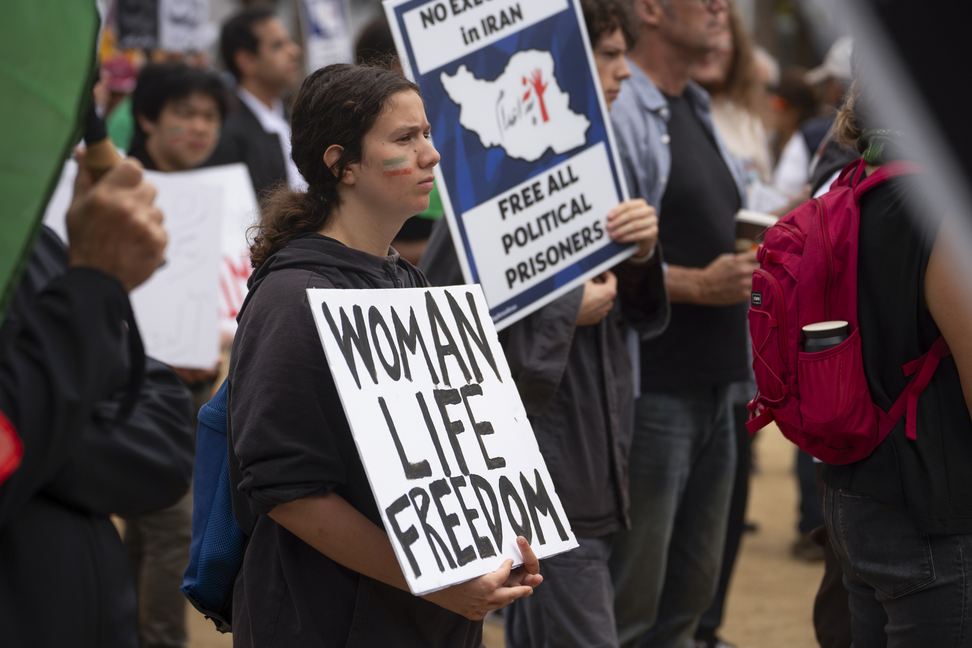 A person holds a sign reading "Woman Life Freedom" in a group of people.