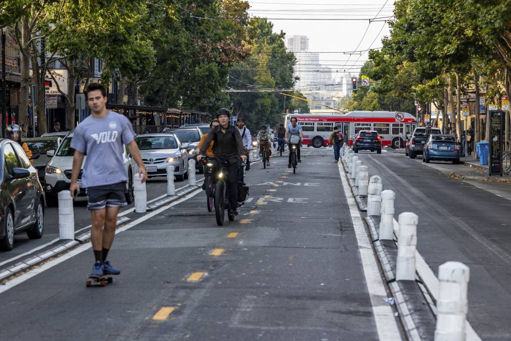 People on bikes and skateboards ride down a bike path in the middle of a city street.