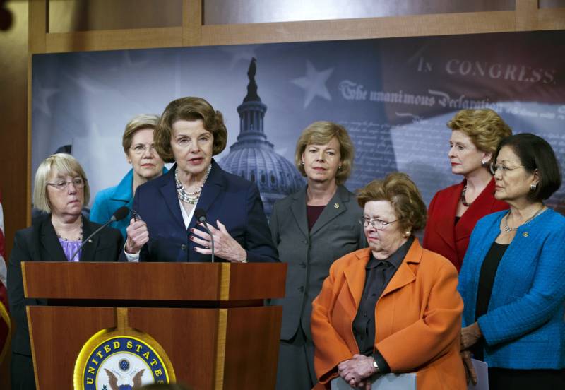 Sen. Dianne Feinstein stands at a podium, surrounded by other female senators.