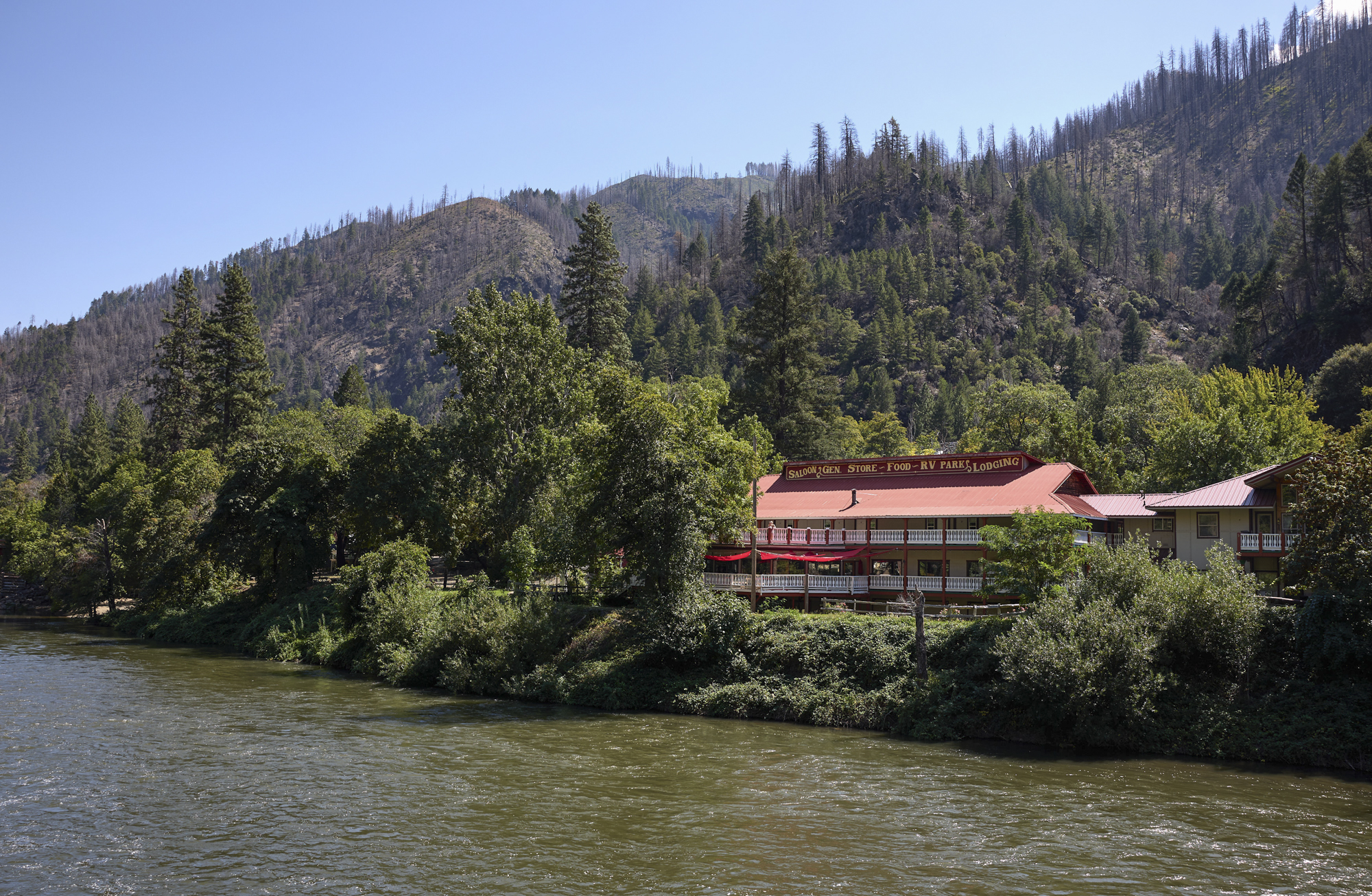 a building with a red roof sits among trees alongside a river