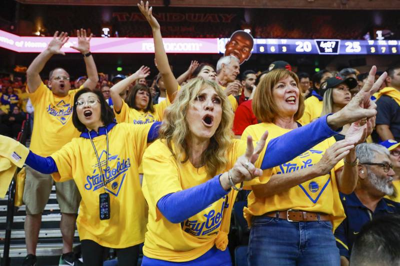 Several women wearing yellow and blue t-shirts cheer and wave inside a sports arena.
