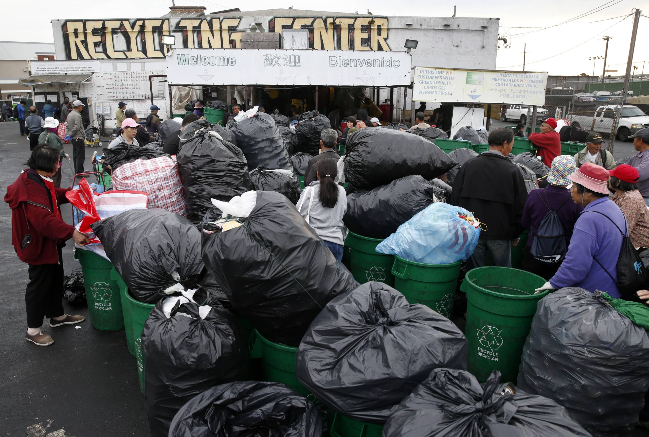 people lined up outside a recycling center with trash bags full of recyclable bottles and cans