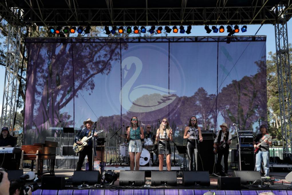 Eight people are seen on stage, with several holding different musical instruments.
