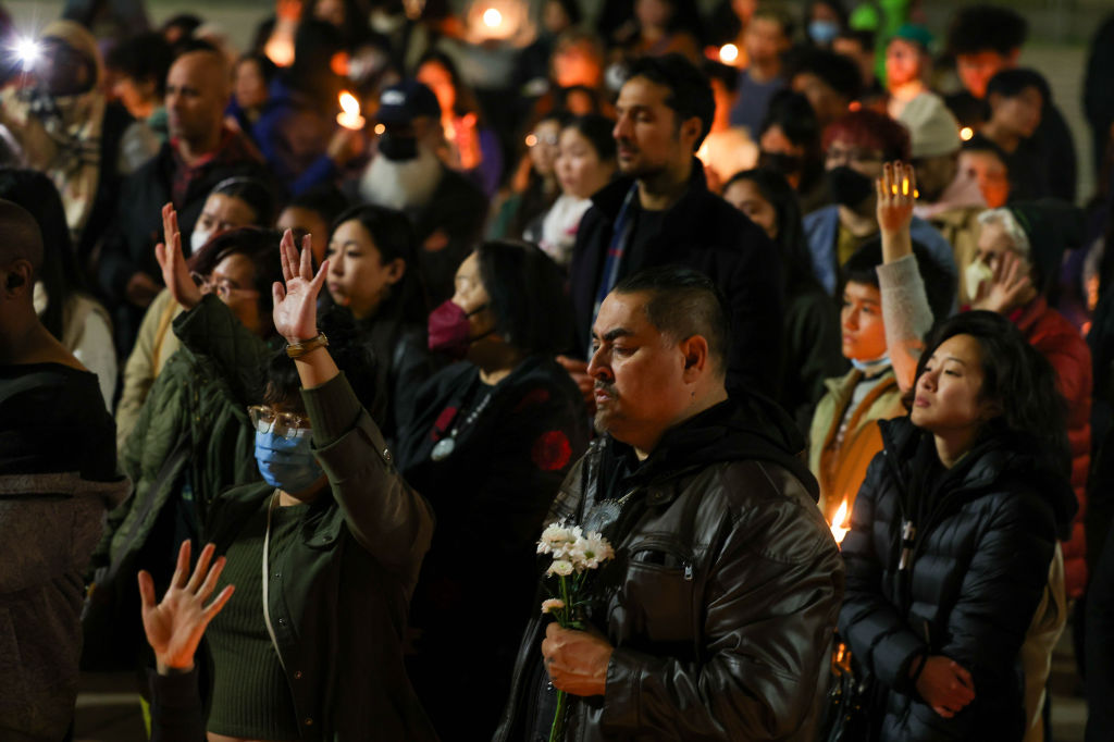 A crowd of people holding signs and candles at night, some praying with eyes closed.