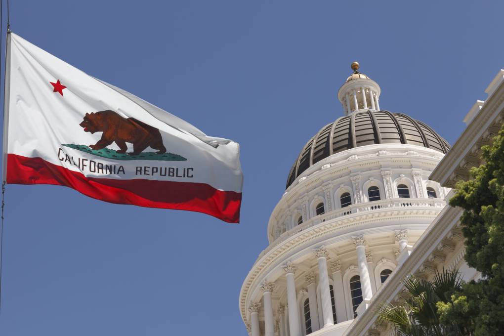 The California state flag with the Capitol cupola in Sacramento behind it.