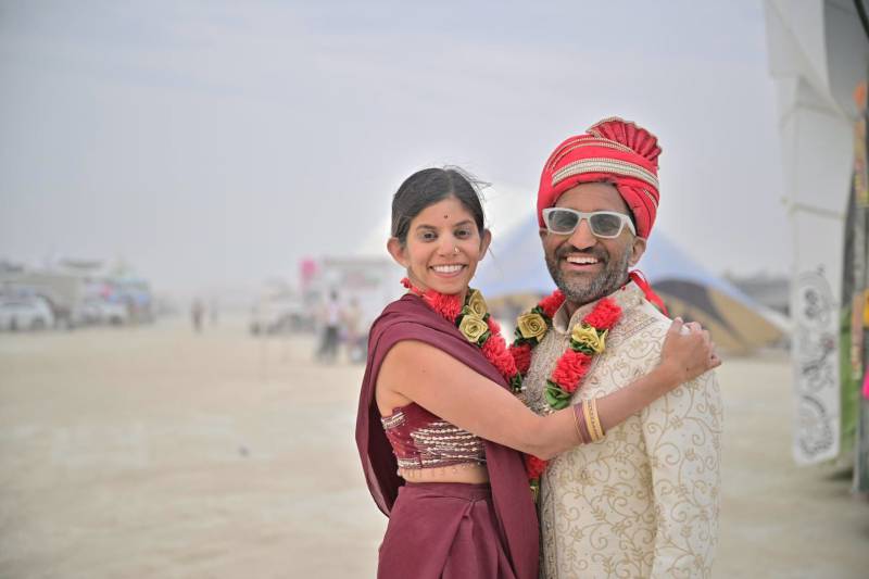 Two people stand dressed in Indian clothes with sand in the background.