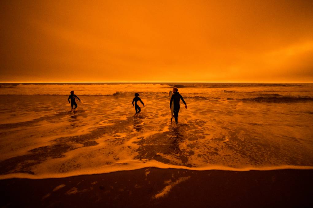 A silhouette of three people in the ocean with an orange-colored sky.