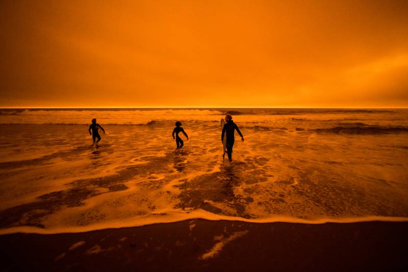 A silhouette of three people in the ocean with an orange-colored sky.