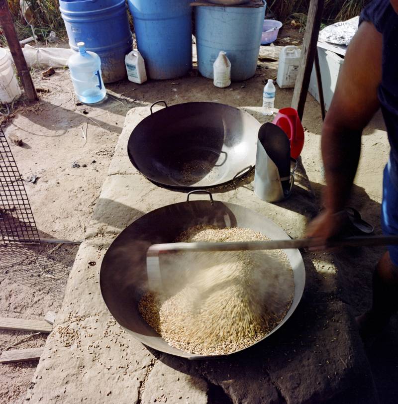 A hand stirs a large wok filled with grain.