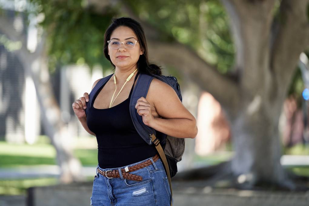 A woman wearing glasses, a black shirt and a backpack stands outside.