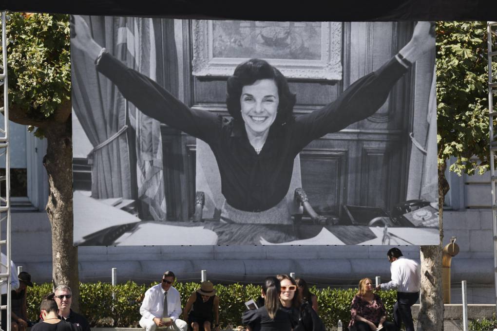 Mourners gather in front of a large black and white image of the late senator.