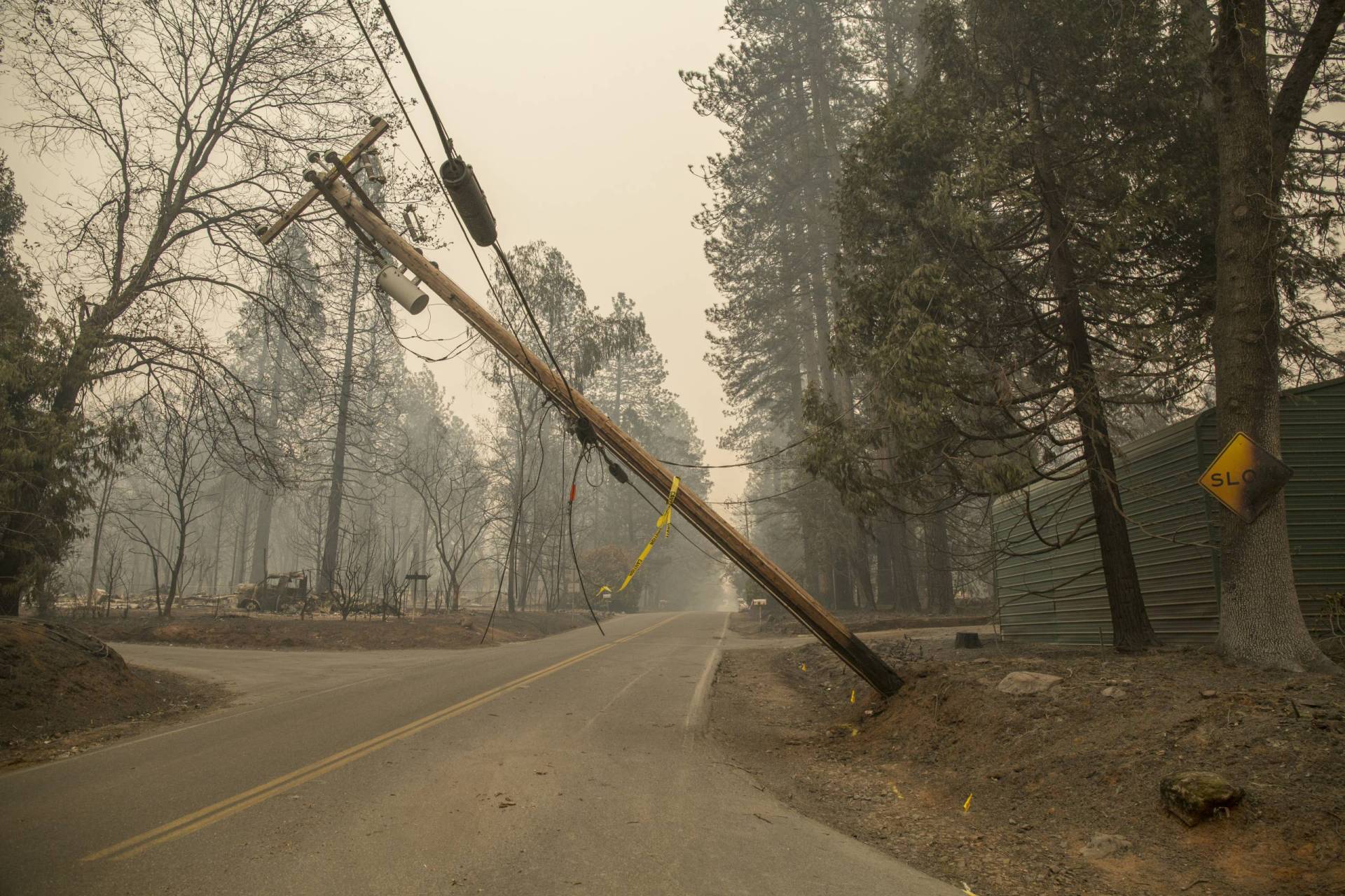 Telephone pole tipped over, pulling down wires, amid smoky air