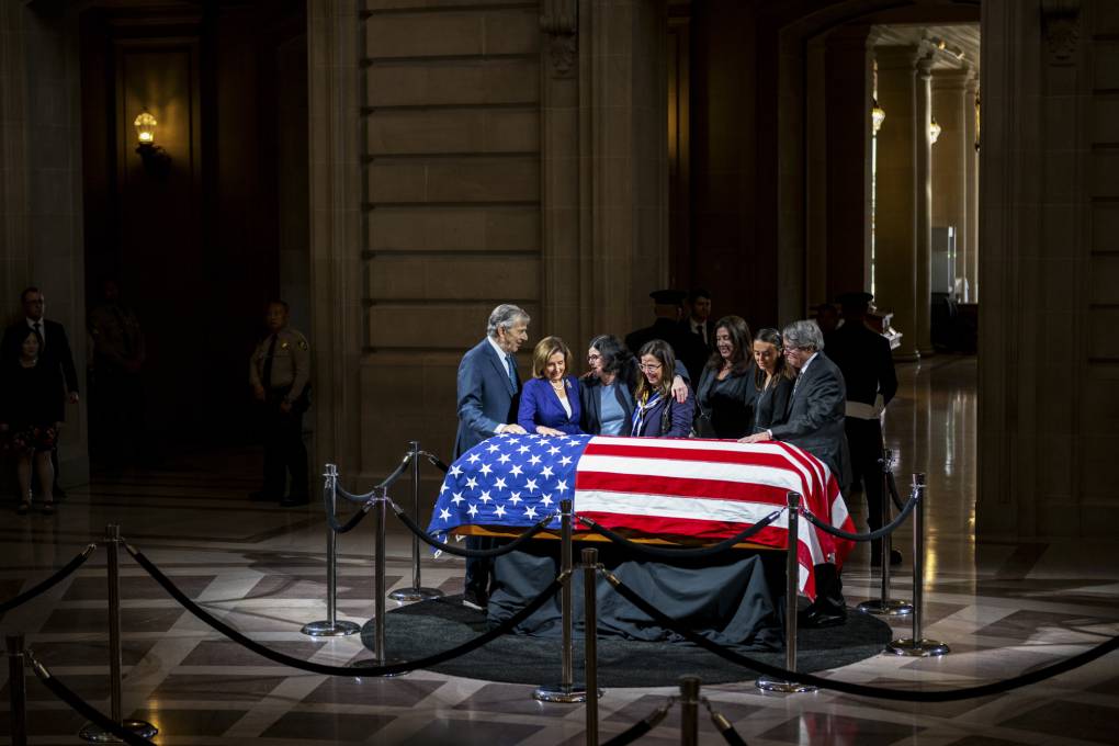 A small group of people surrounds a casket draped in an American flag inside an ornate building.