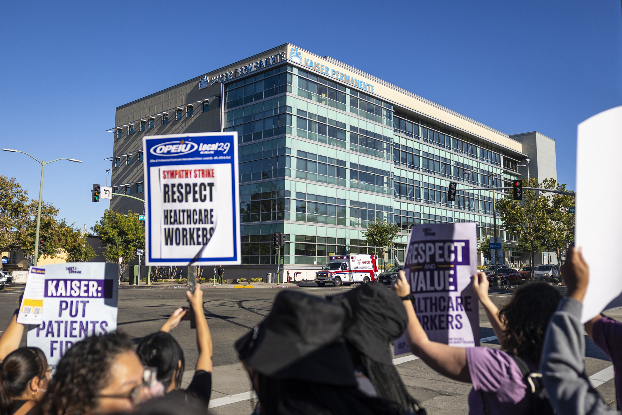 A group of people hold signs in front of a large modern looking building.