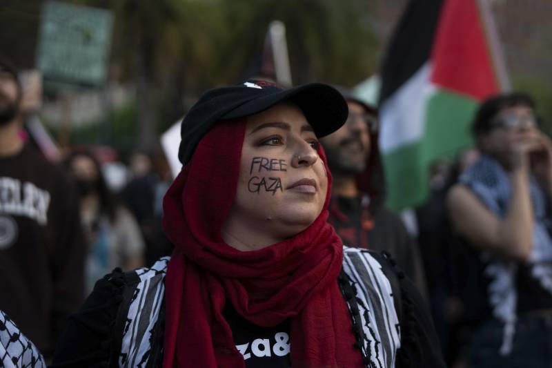 A person wearing a red headscarf with "Free Gaza" written on their cheek.
