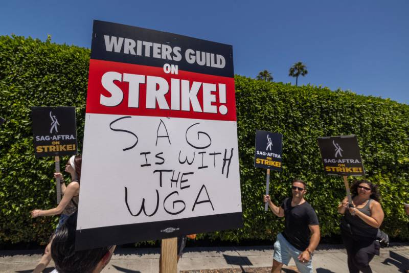 SAG-AFTRA on STRIKE sign with protestors in the back holding the same signs.