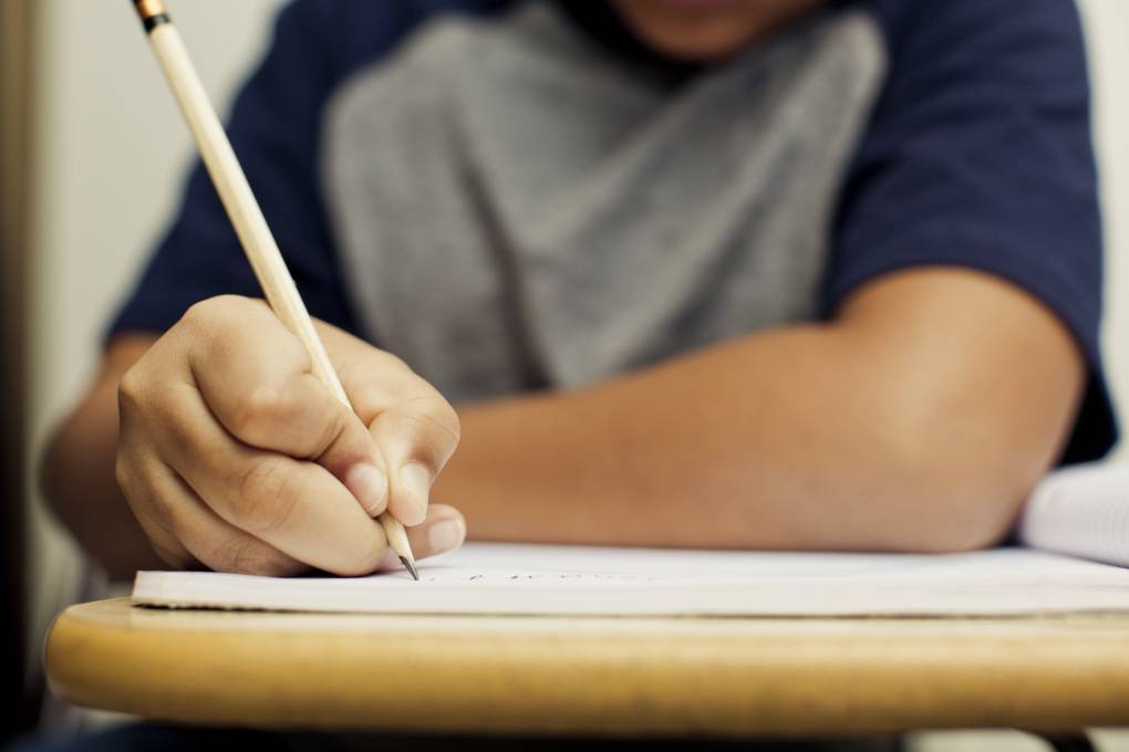 A child writing at a desk in class with a pencil.