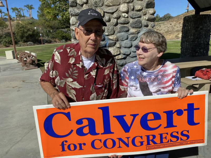 an older white man and woman in sunglasses hold a sign that reads 'Calvert for Congress'