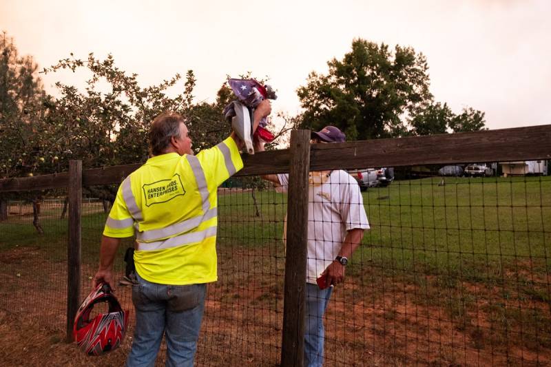 A man wearing neon yellow shirt with silver stripes hands another man a flag over a fence.