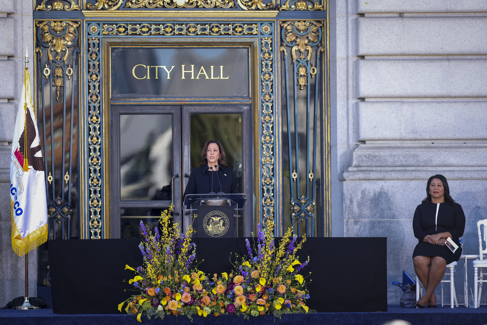 Woman speaks at lectern in front of building