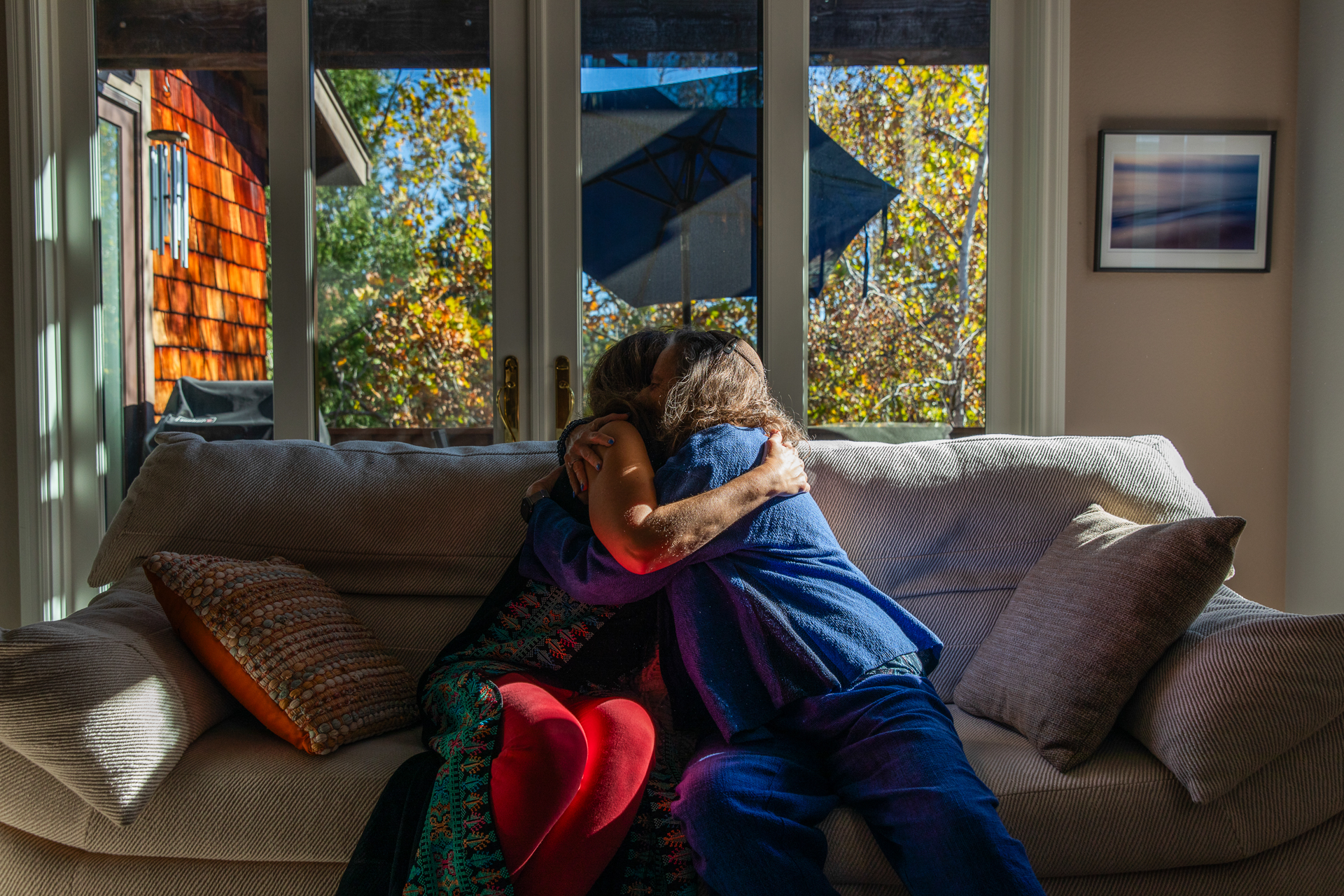 Two women hug each other while sitting on a couch in a home.