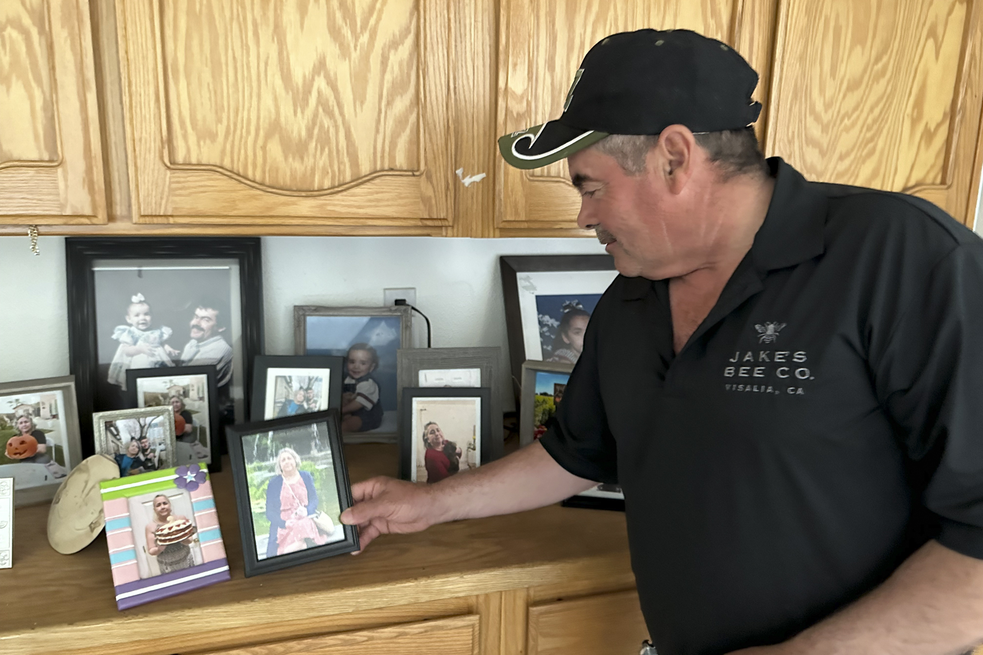 A person in a baseball cap looks at photos on a shelf inside a home.