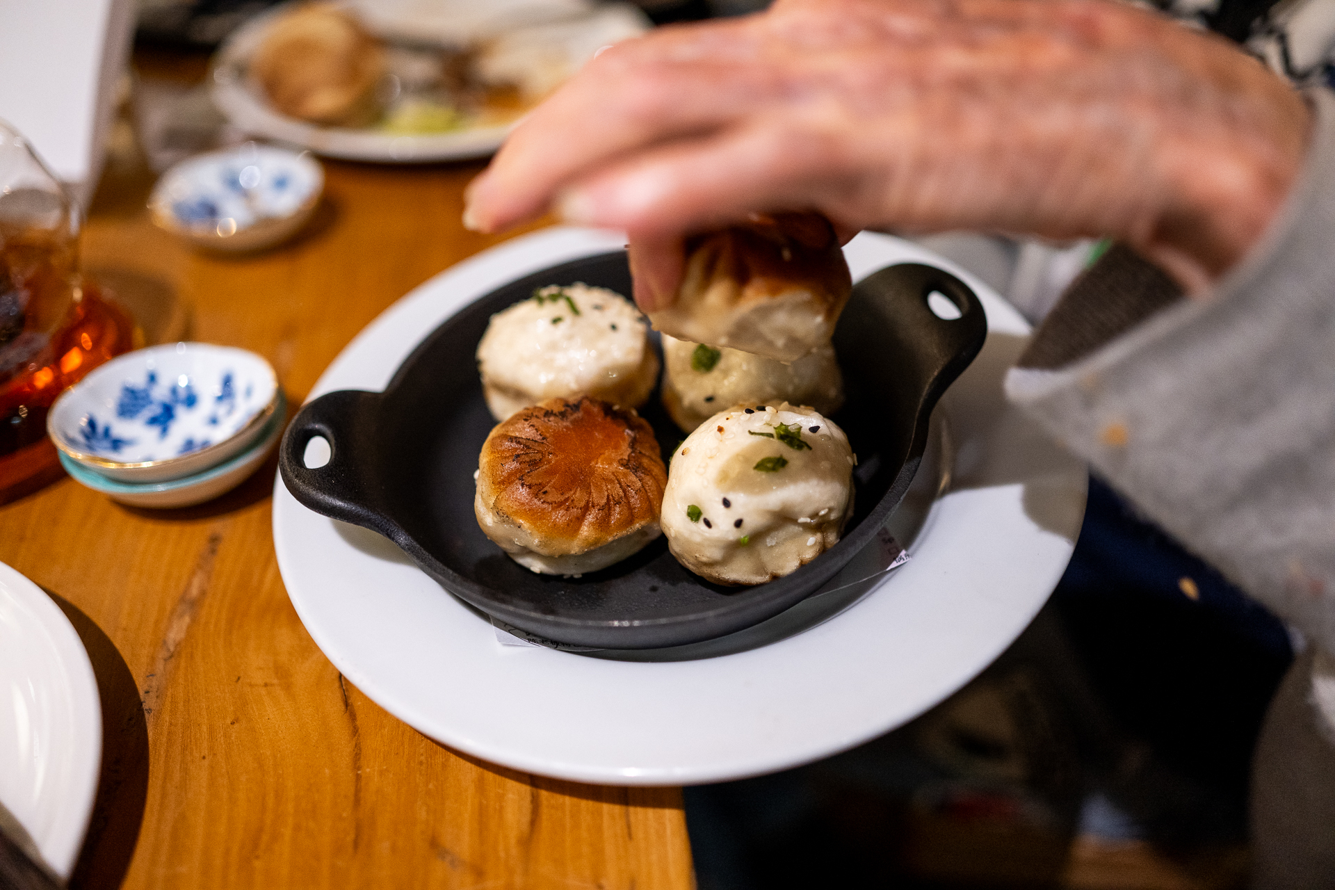 A hand reaches for one of five dumplings on a dish.