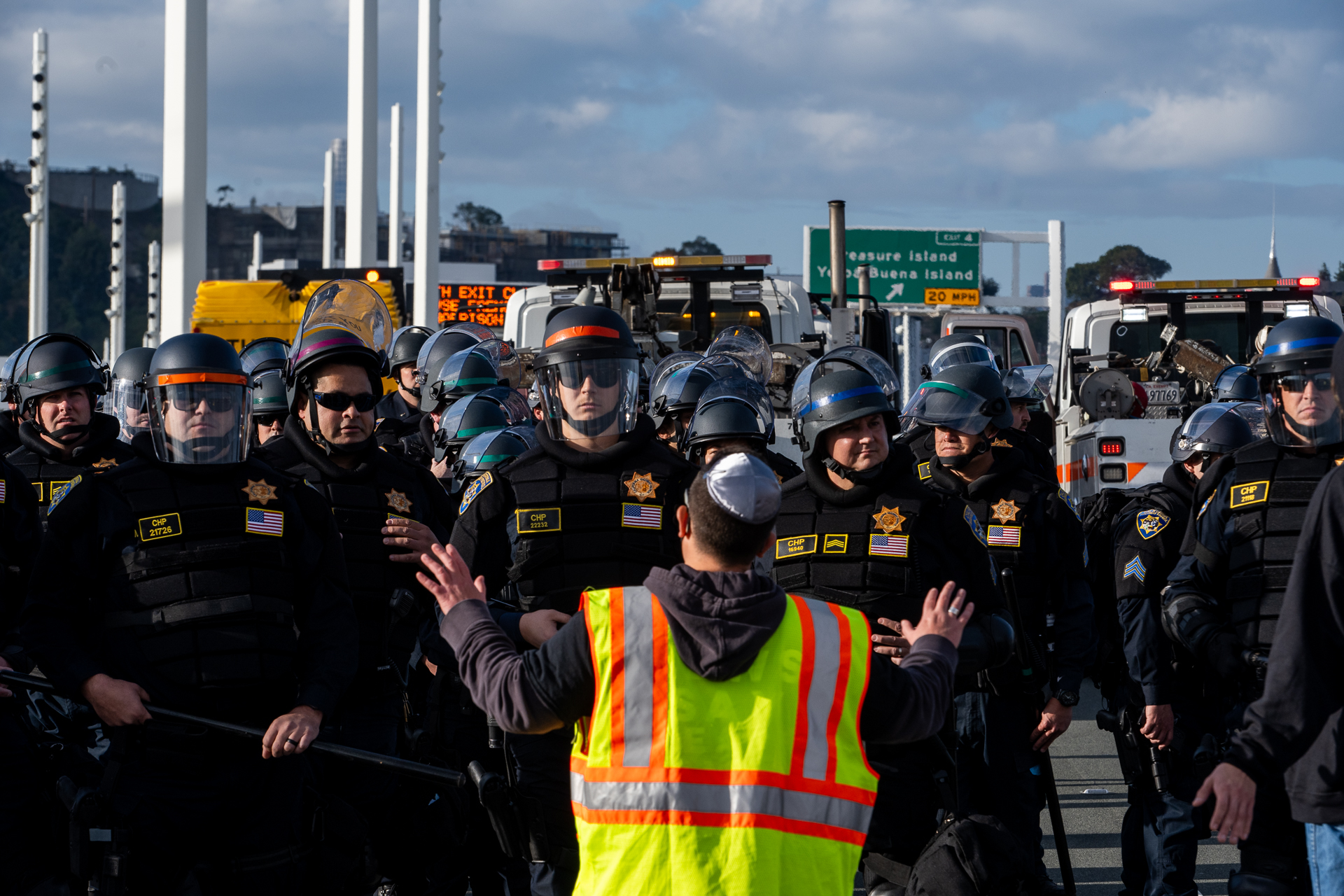 A person raises their arms wearing a reflective vest with a line of police in front of them.
