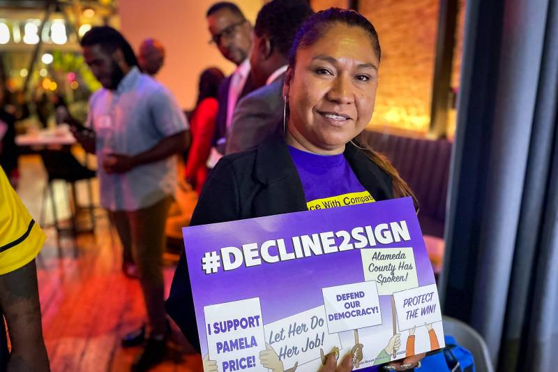 A woman holds a purple and white sign.