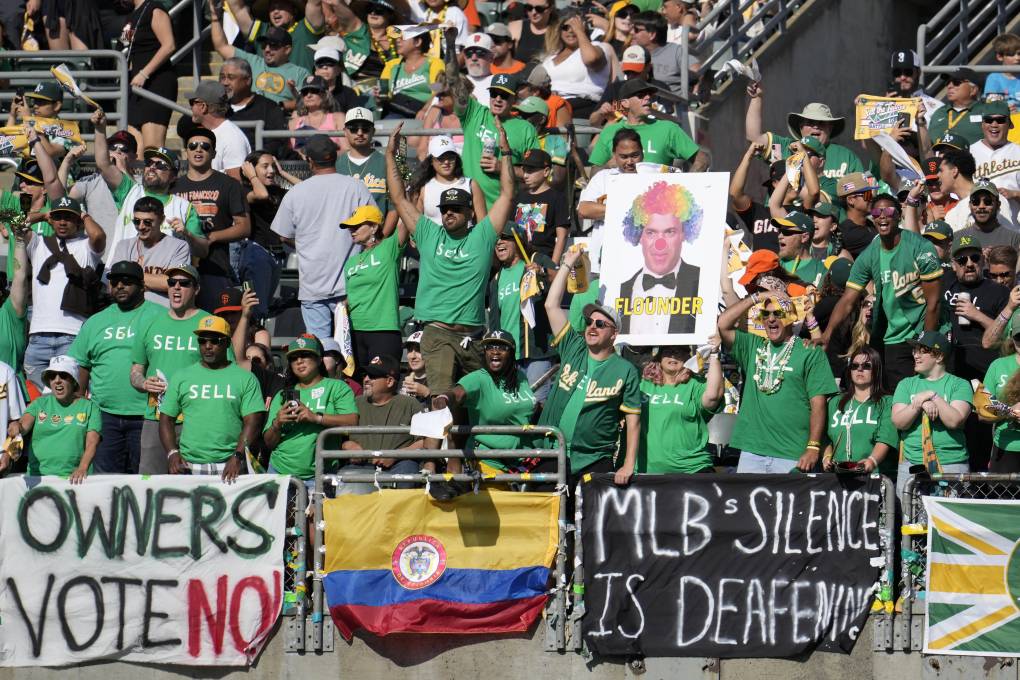 A large group of people in a sports arena, mainly wearing green, are draping signs over a barrier that read, "Owners vote no!" and " MLB's Silence is Deafening."
