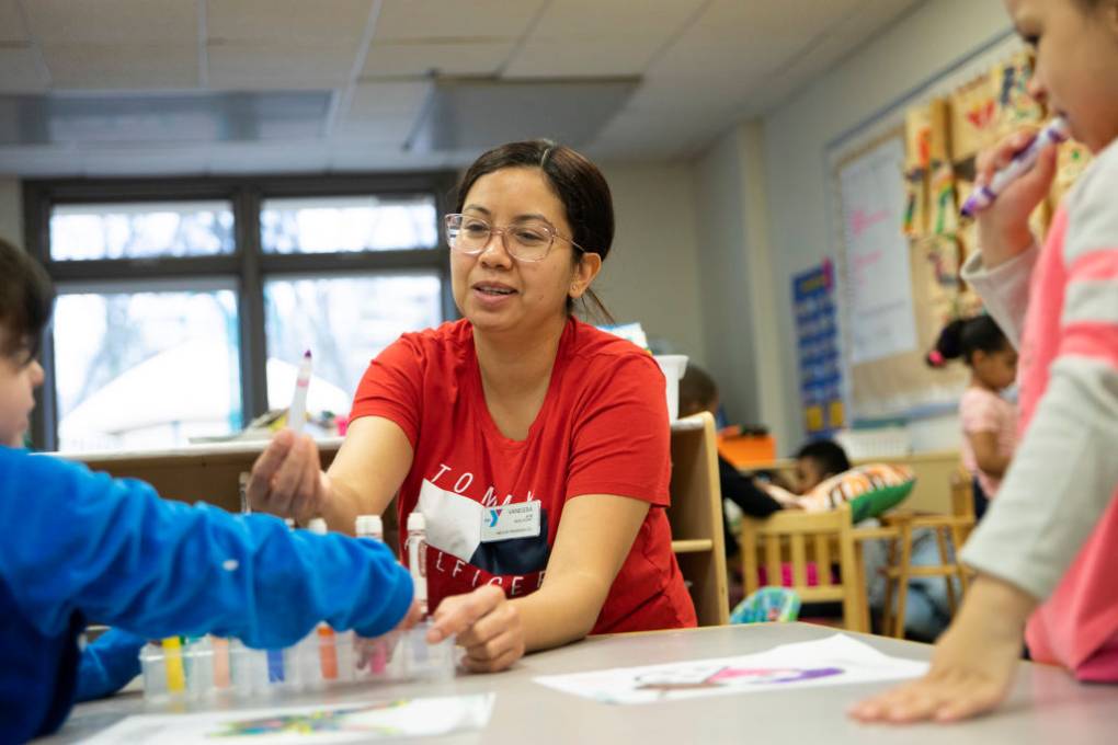 A young Latina woman working with kids in a classroom.