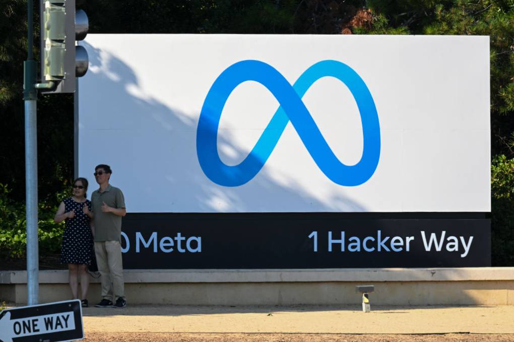 Two people stand in front of a big Meta sign as they pose for a photo.