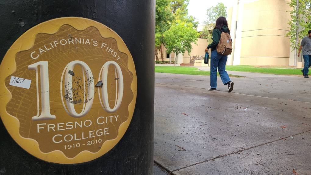 A student with a backpack walks past a sign on a pole that says, 'California's First 100 - Fresno City College - 1910-2010.'