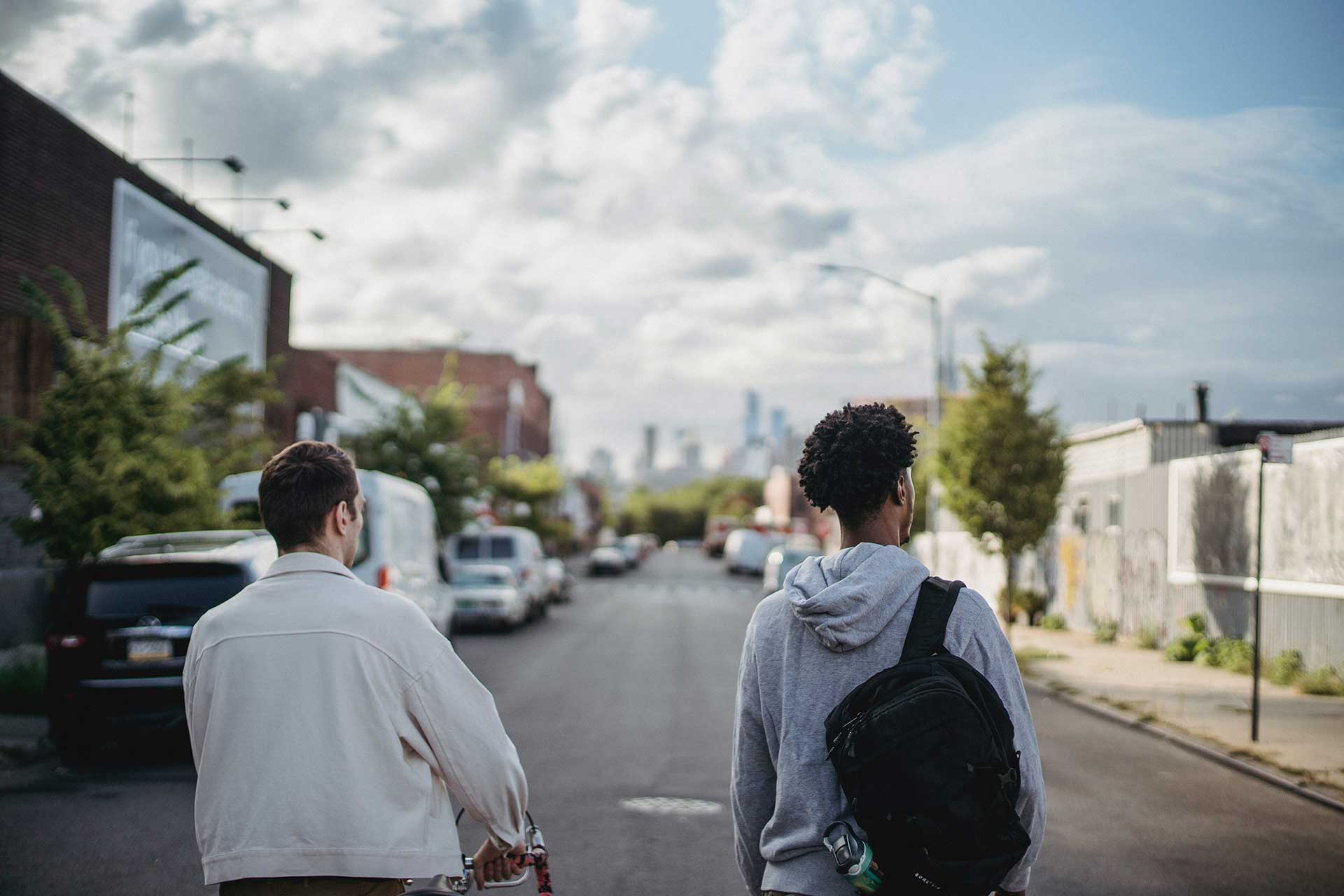 Two figures, photographed from behind, walk on a wide city street.